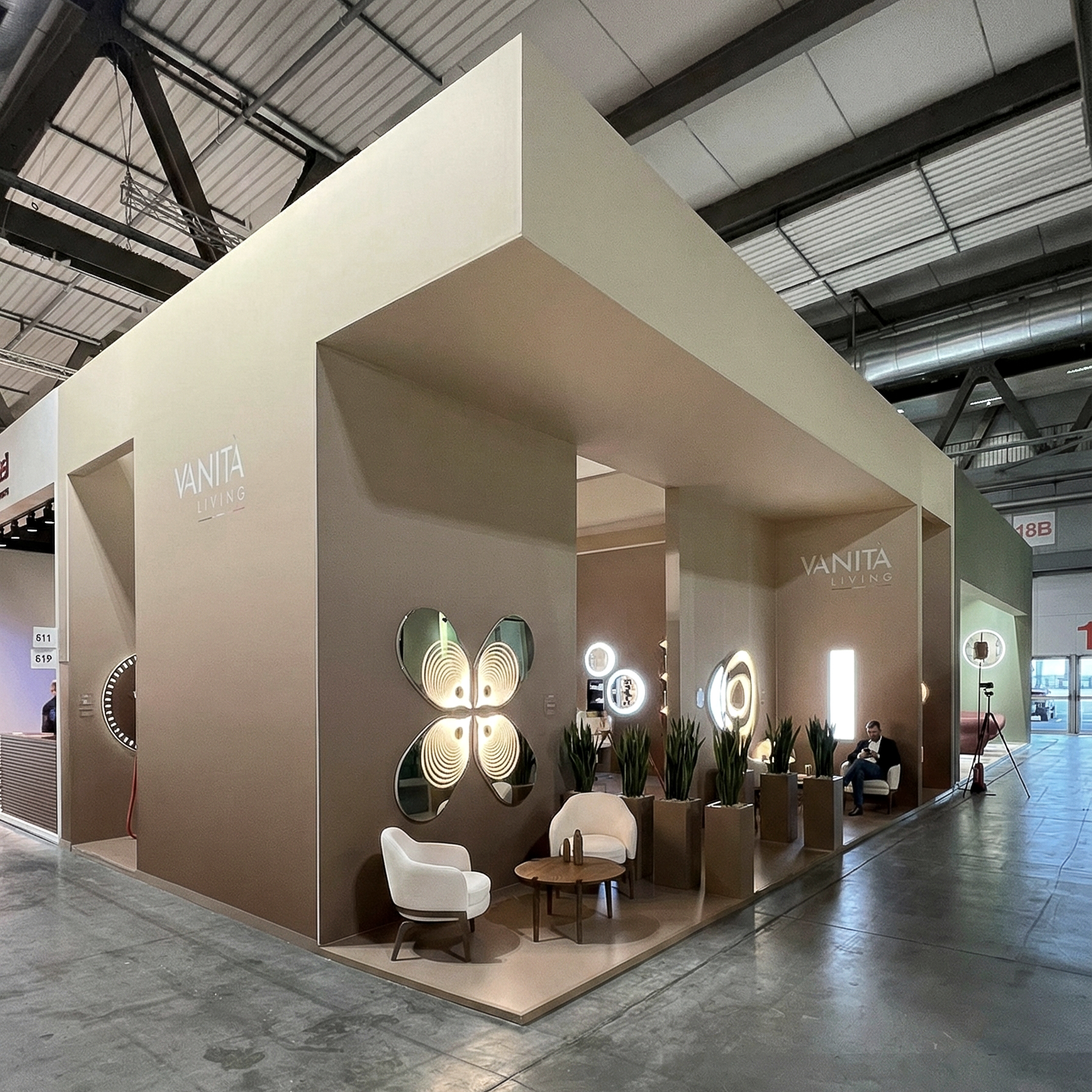 Vista frontale dello stand Vanità Living con logo centrale e apertura laterale che mostra la parete espositiva degli specchi.