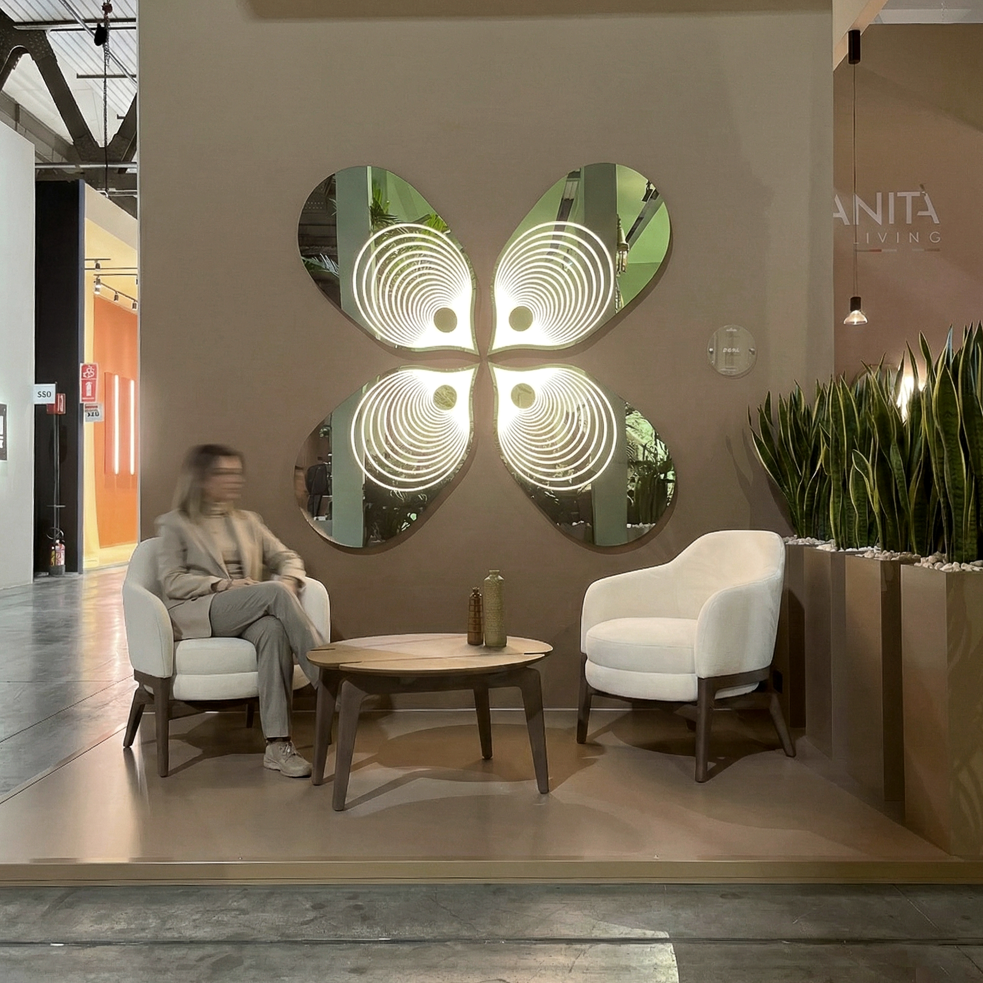 Lounge esterna con due poltrone, tavolino e grande specchio a quattro elementi con motivo luminoso concentrico.