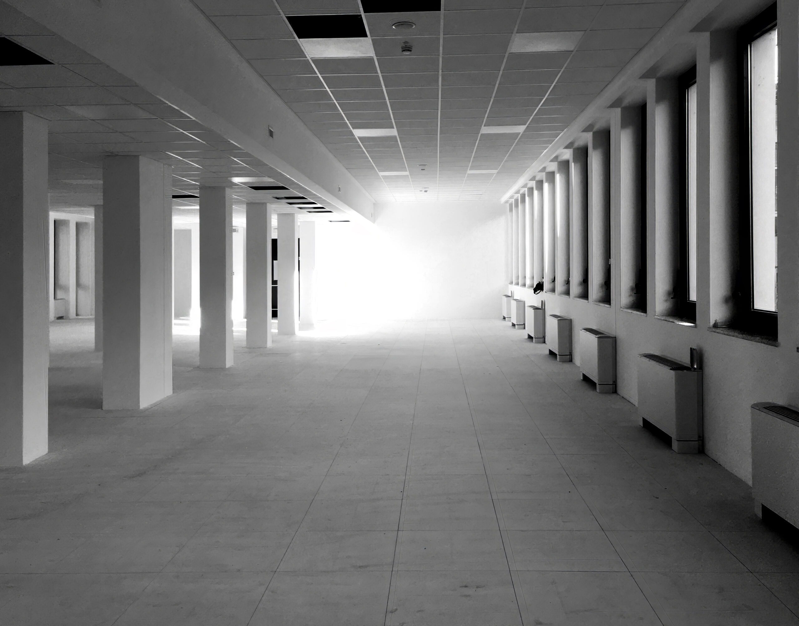 Grande open space vuoto con colonne e finestre perimetrali, stato di fatto iniziale degli uffici Terumo Neuro a Milano prima del progetto di interior design.