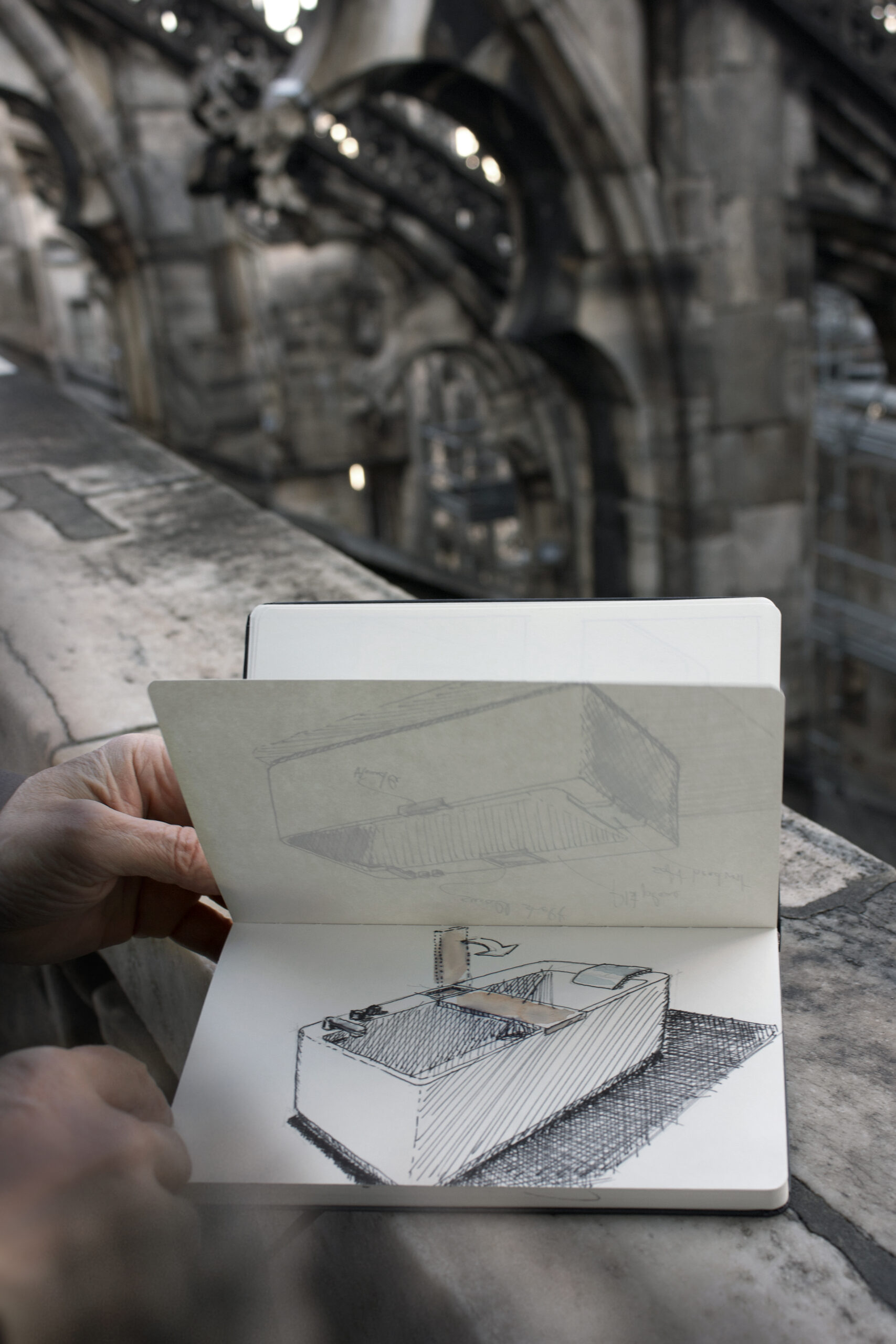 Taccuino aperto con schizzo prospettico della vasca Infinity tenuto in mano davanti a un’architettura storica in pietra sfocata sullo sfondo.